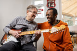 Two men playing electric guitars together in a sunlit lounge at Cae Deri