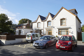 Street view of Isfryn, a white rendered house with cars parked on the front forecourt