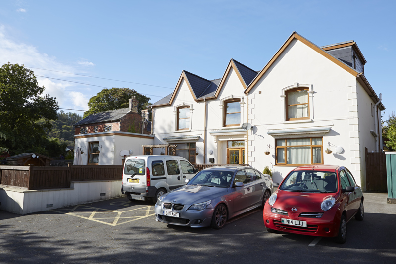 Street view of Isfryn, a white rendered house with cars parked on the front forecourt