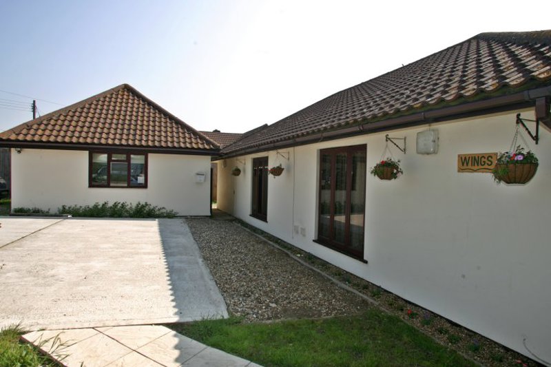 White-rendered single-storey exterior of Wings with a tiled roof, hanging baskets and a Wings name sign