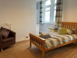Bedroom at Princes Court with a wooden bed, bedside lamp, brown leather tub chair and arched windows