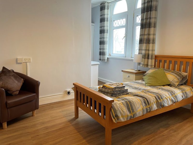 Bedroom at Princes Court with a wooden bed, bedside lamp, brown leather tub chair and arched windows
