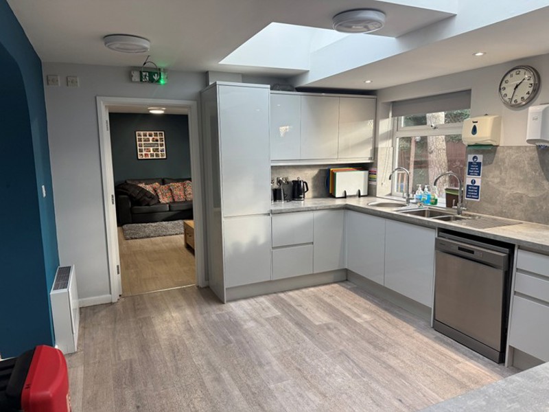 Kitchen at Pinetrees with white gloss units, a skylight and an opening through to the lounge