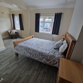 Spacious bedroom at Birchwood House with an oak double bed, armchair and two curtained windows