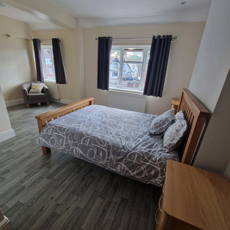 Spacious bedroom at Birchwood House with an oak double bed, armchair and two curtained windows