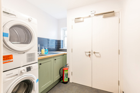 Laundry room at Brynawel with a stacked washer and dryer, sage green units and a blue tiled splashback