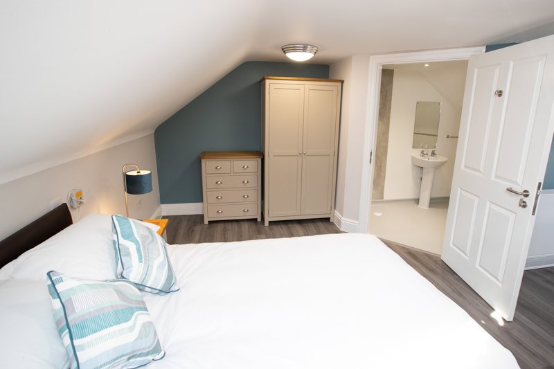 Loft bedroom at Willow Lodge with a double bed, cream wardrobe and an ensuite wet room through the door