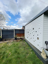 Light grey garden shed with mirrored decorations next to a lawned garden