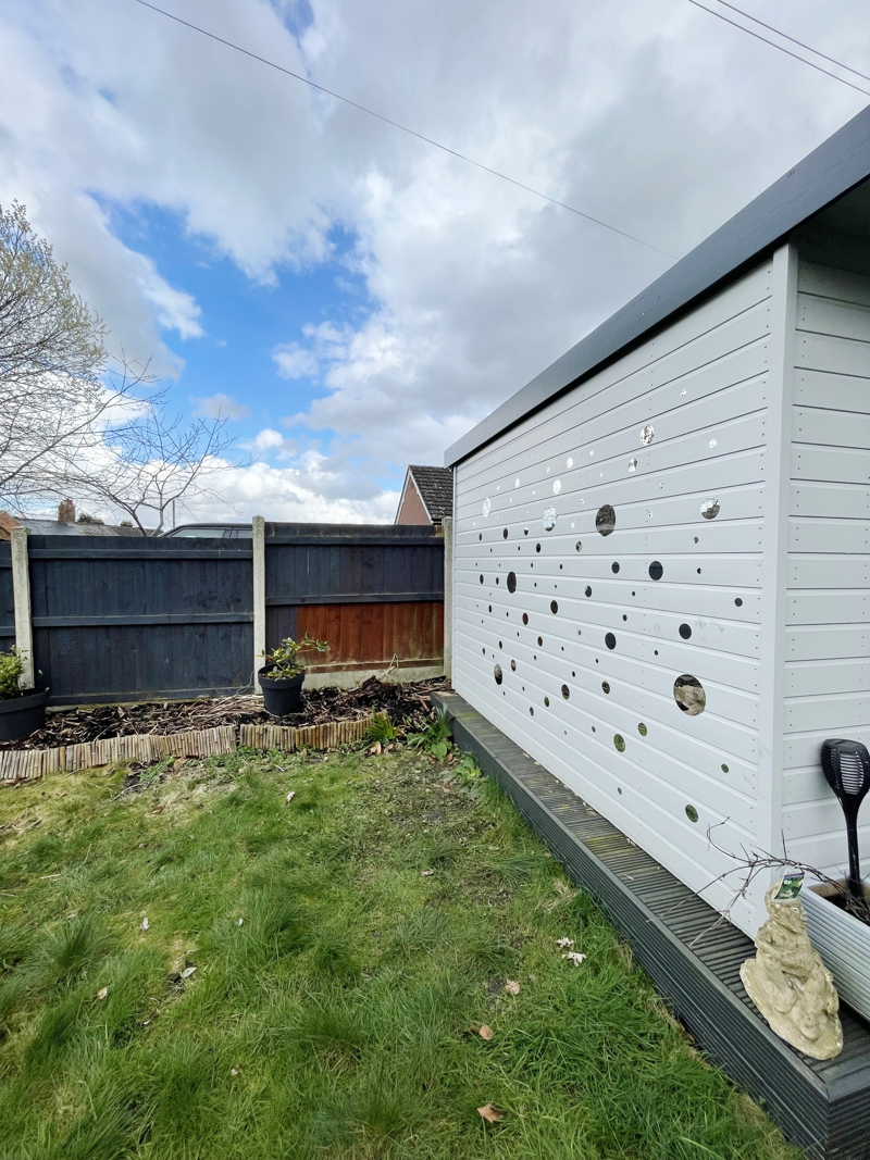 Light grey garden shed with mirrored decorations next to a lawned garden