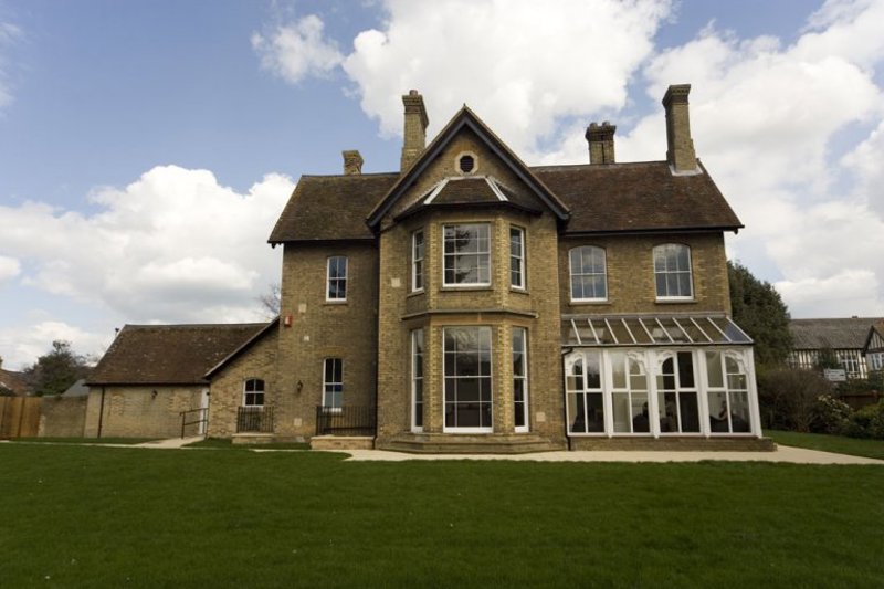 Front exterior of Sheridan House, a large yellow-brick Victorian house with a bay window, conservatory and lawn