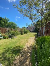 Rear garden at Eilat with a lawn, brick path, birdbath and planted borders under a blue sky