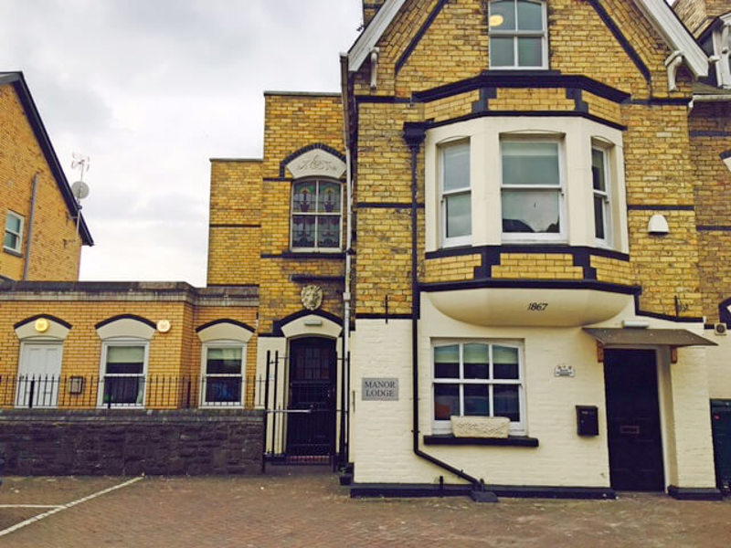 Yellow-brick Victorian front of Manor Lodge with a bay window and 1867 datestone