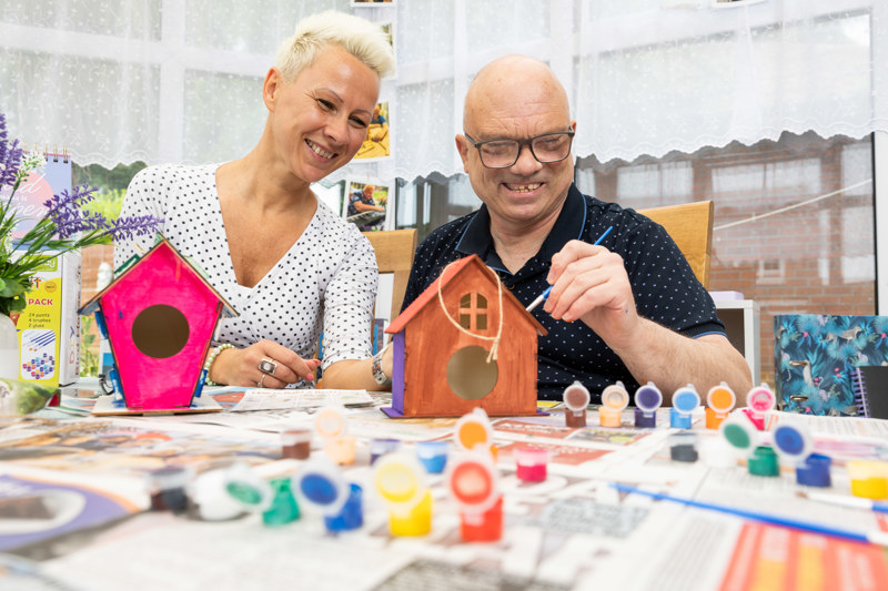 Two people painting wooden birdhouses at a craft table at Brookside Avenue East