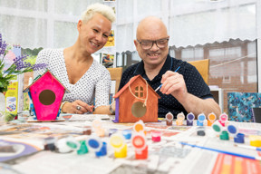 Two people painting wooden birdhouses at a craft table at Brookside Avenue East