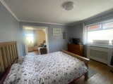 Bedroom at Rosewood with a wooden double bed, a chest of drawers with a TV and a bright window
