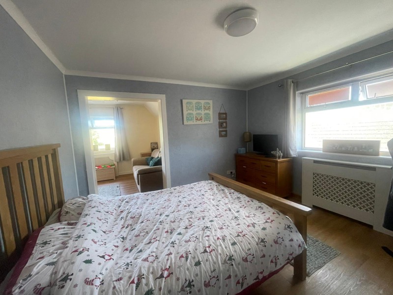 Bedroom at Rosewood with a wooden double bed, a chest of drawers with a TV and a bright window