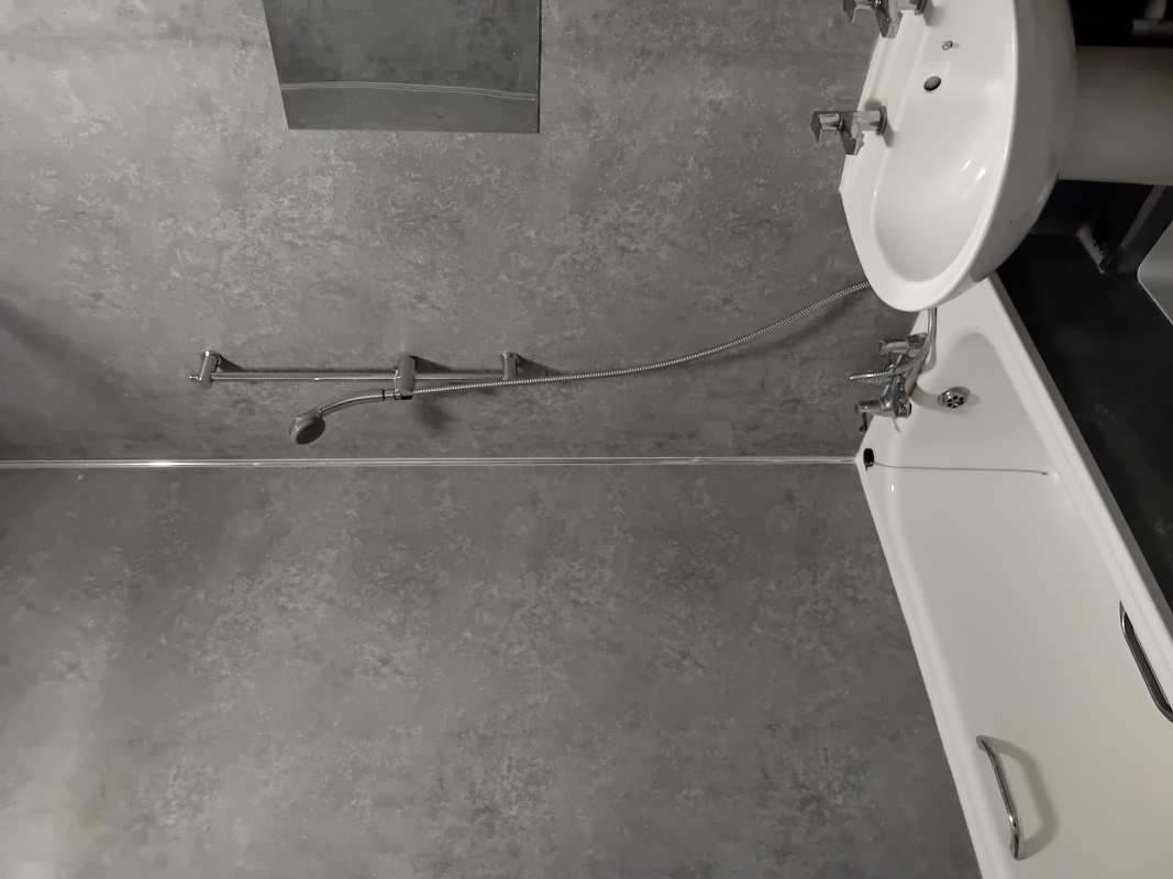 Bathroom at Eynesbury House with a bath, basin and a wall-mounted shower over grey tiling