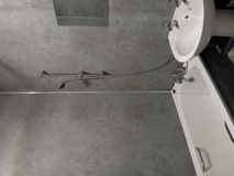 Bathroom at Eynesbury House with a bath, basin and a wall-mounted shower over grey tiling
