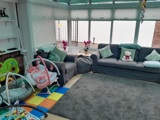 Bright conservatory living room at Victoria Villas with grey sofas, a baby bouncer and colourful play mats