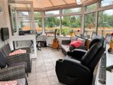 Conservatory lounge at Chesterwood with rattan and leather seating, a guitar and garden views