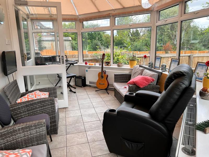 Conservatory lounge at Chesterwood with rattan and leather seating, a guitar and garden views