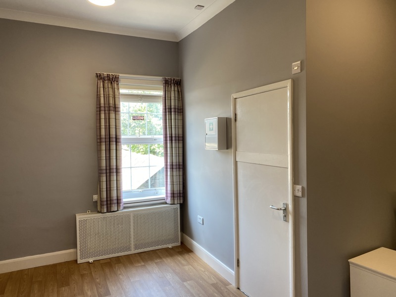 Bedroom at Cranwell Court with a curtained sash window, radiator cover and first aid cabinet