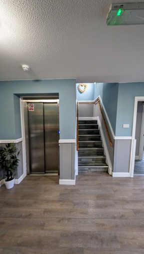 Lift and staircase at Cedar House with handrails in a blue-painted hallway