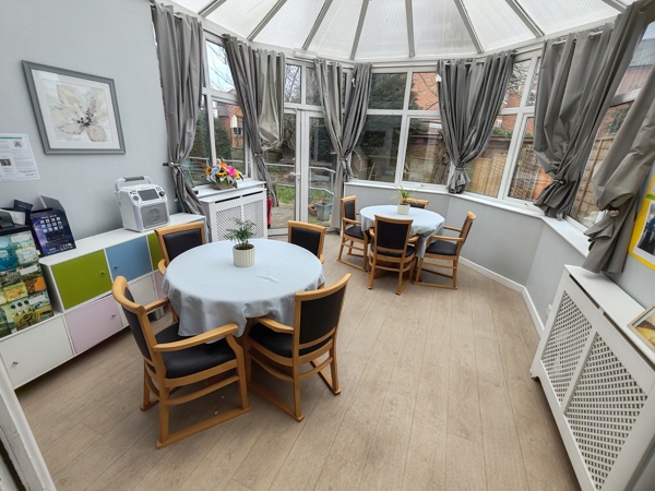 Conservatory dining area at Evergreen with round tables, chairs and a glazed roof overlooking the garden