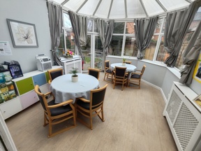 Conservatory dining area at Evergreen with round tables, chairs and a glazed roof overlooking the garden
