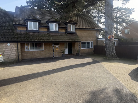 Front exterior of Pinetrees, a yellow-brick house with dormer windows and a gravel driveway