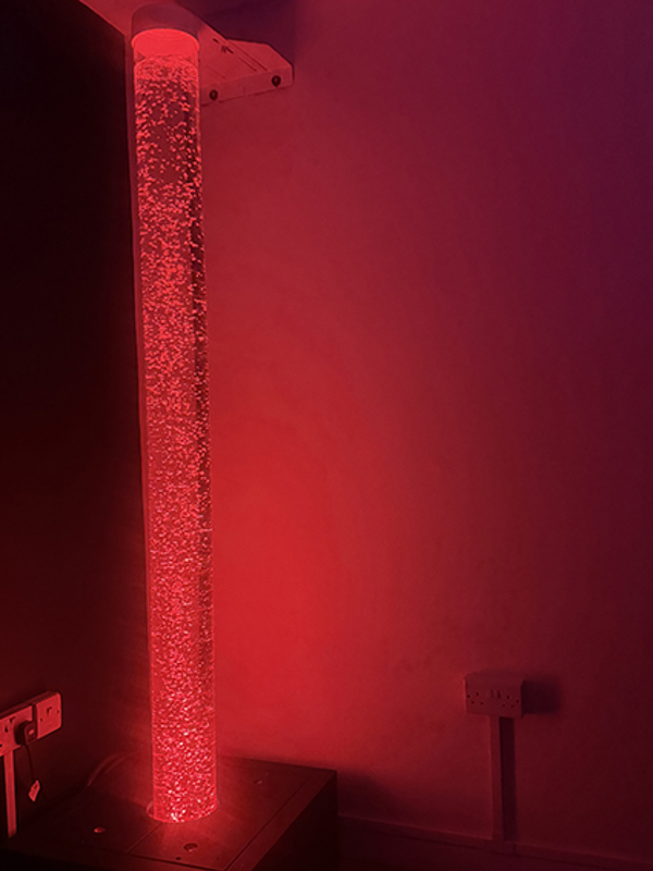 Sensory bubble tube glowing red in the corner of a sensory room at Pinetrees