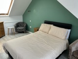 Bedroom at Thompson Court with a double bed, green feature wall, sloped attic ceiling and a tub chair