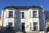 White-rendered detached exterior of Pen Bryn with bay windows and a slate roof under a blue sky
