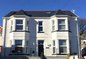 White-rendered detached exterior of Pen Bryn with bay windows and a slate roof under a blue sky