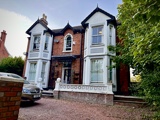 Front exterior of Glanmore, a Victorian red brick house with white bay windows and a gravel driveway