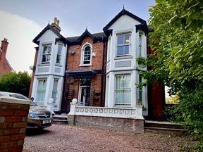 Front exterior of Glanmore, a Victorian red brick house with white bay windows and a gravel driveway