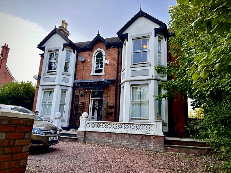 Front exterior of Glanmore, a Victorian red brick house with white bay windows and a gravel driveway