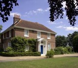 Front exterior of Ganwick House, a red-brick double-fronted house with a blue front door and columned porch set in lawned grounds