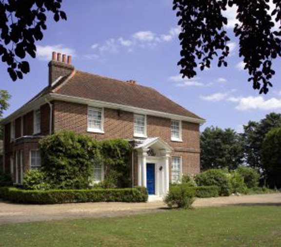 Front exterior of Ganwick House, a red-brick double-fronted house with a blue front door and columned porch set in lawned grounds