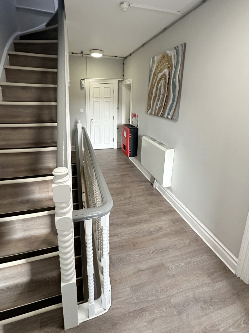 Light coloured hallway with staircase and artwork on the walls.