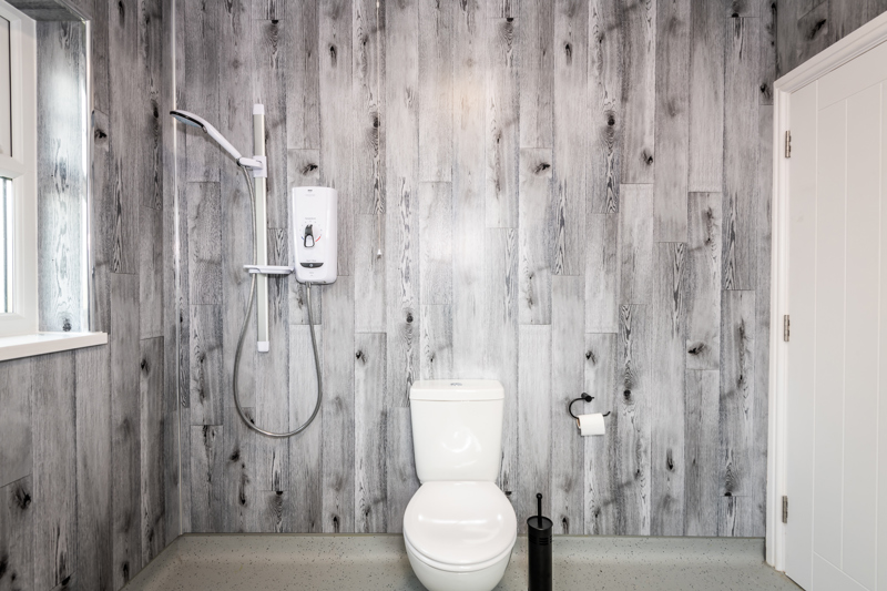 Wet room at Brynawel with grey wood-effect panelling, an electric shower and a toilet