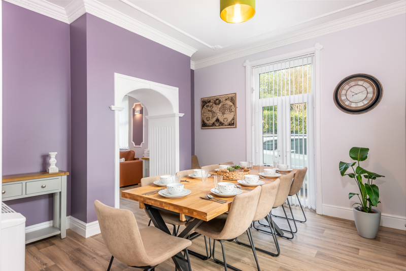 Dining room at Brynawel with a wooden table set for a meal, beige chairs and lilac walls