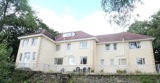 Exterior of Taith Cartref, a large cream-rendered care home with a tiled roof, patio seating and surrounding trees