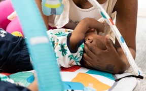 Parent playing with a baby on a colourful play mat under a baby gym at Crown House family assessment centre