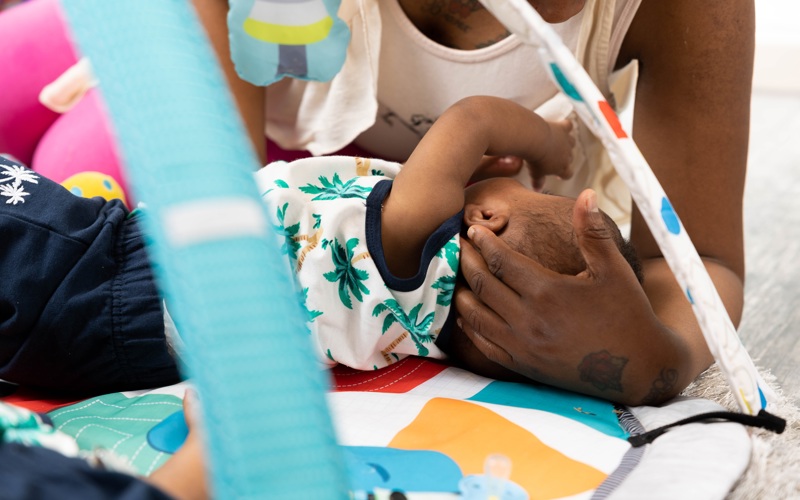 Parent playing with a baby on a colourful play mat under a baby gym at Crown House family assessment centre