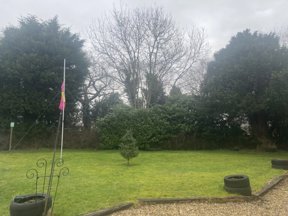 Garden at Maple Leaf Lodge with a lawn, flagpole, planted tyres and mature trees