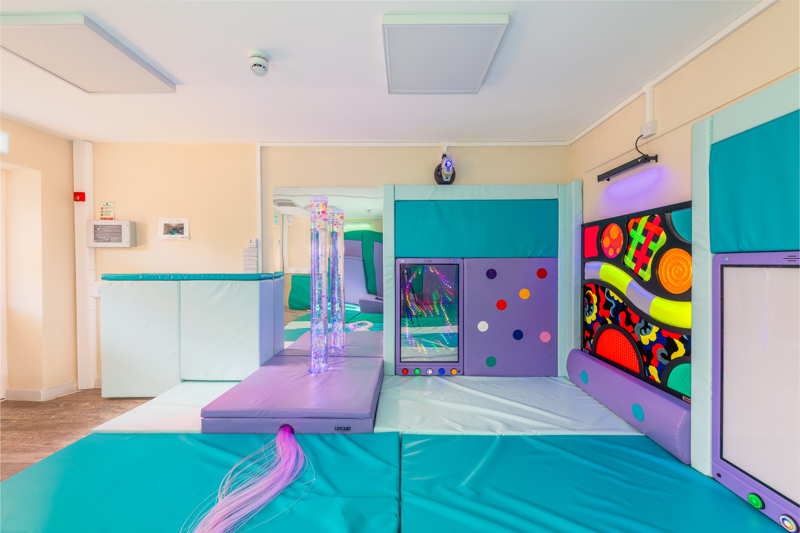 Sensory play room with jade coloured matts, purple elements and a brightly coloured and patterned wall.