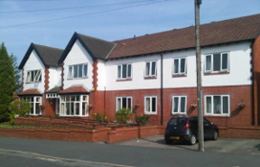 Front exterior of Byron Lodge, a white and red-brick two-storey care home with on-street parking