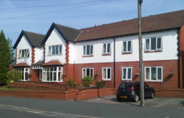Front exterior of Byron Lodge, a white and red-brick two-storey care home with on-street parking