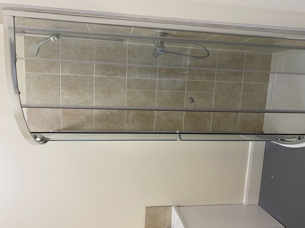 Quadrant shower enclosure with beige tiling and sliding glass doors at Cranwell Court